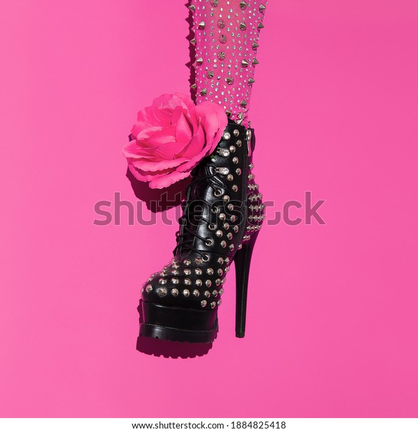 Fashion leg in heel\
black boots and pink roses on minimal pink background. Stylish\
accessories shoes\
concept