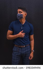 Fashion Lifestyle, Portrait Of A Young Latino Man On A Black Wall. Blue Polo Shirt And Plaid Pants. In A Pandemic With A Mask