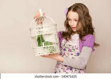 Fashion Little Girl Looks On Birdcage. Studio Photo