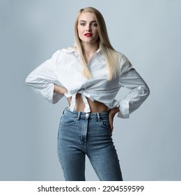 Fashion And Make-up Concept. Beautiful And Sexy Long Hair Blonde Woman With Classic Outfit And Red Lipstick Studio Portrait. Slim Model Wearing Blue Jeans And White Blouse. Toned Image In Blue Color