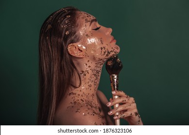 Fashion makeup concept. Beauty, fashion gold concept. Portrait of a beautiful girl model with gold on her skin is holding brush.