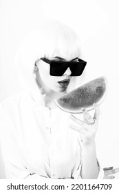 Fashion, Make-up, Food Concept. Close-up Studio Shot Of Fancy And Beautiful Looking Woman With White Wig And Big Sunglasses Holding Slice Of Red Watermelon In Her Hands. Black And White Image