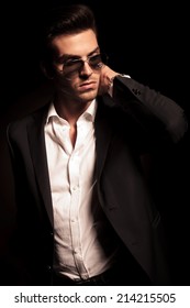 fashion man in suit and sunglasses holding the back of his neck and looks to his side on black background