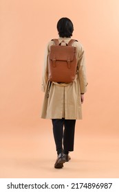 Fashion Model. Back View Young Man With Hairstyle In Coat With Backpack Walking On Brown Background

