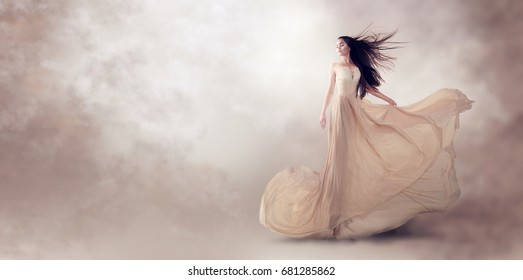 Fashion model in beautiful luxury beige flowing chiffon dress, Woman in long flying evening dress with a gown, Stunning fantasy model. Silk fabric waving on wind. Satin Cloth Flowing, Waves of a dress