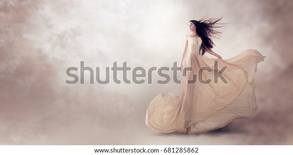 美しい豪華なベージュの流れるシフォンのドレスのファッションモデル 長い空飛ぶイブニングドレスの女性 ガウン 魅力的なファンタジーモデル 風になびく 絹織物 サテンの布が流れ ドレスの波 の写真素材 今すぐ編集