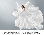 Fashion Model in Creative Pure White Dress as Cloud. Woman in Long Silk Gown with Chiffon Fabric flying on Wind over Light Gray Background. Art Fantasy dancing Girl