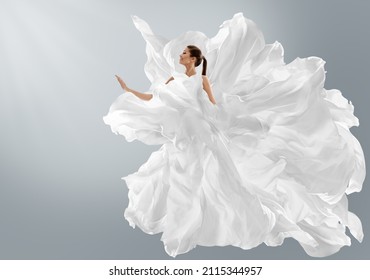 Fashion Model in Creative Pure White Dress as Cloud. Woman in Long Silk Gown with Chiffon Fabric flying on Wind over Light Gray Background. Art Fantasy dancing Girl