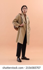 Fashion Model. Full Body Young Man With Hairstyle In Coat ,with Backpack Posing On Beige Brown Background

