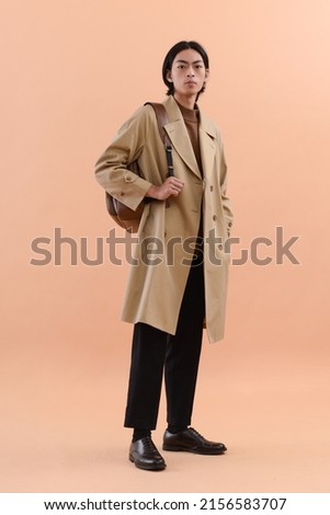 fashion model. full body Young man with hairstyle in coat ,with backpack posing on beige brown background

