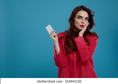 Fashion Model Girl In Stylish Clothes Looking Excited, Shocked And Surprised On Blue Background. Happy Beautiful Sexy Woman In Fashionable Clothing Holding Empty Copy Space Gift Card.  High Resolution