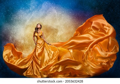 Fashion Model In Golden Dress Over Miracle Night Sky Background. Luxury Woman In Long Silk Gown Dance And Looking At Stars