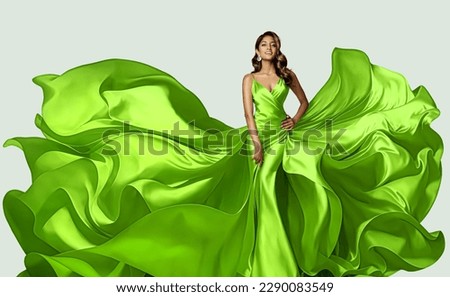 Fashion Model in Green Dress with flying Silk Fabric. Beautiful Girl in Satin Evening Gown over White. Happy Woman in Spring Skirt fluttering on Wind