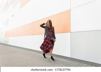 Fashion Model Happy Urban Hipster In Dark Sunglasses With Smile In Fashionable Youth Red-black Outfit And Stylish Sneakers Travel On City. Smiling American Girl Walks Near Modern Wall On Street.