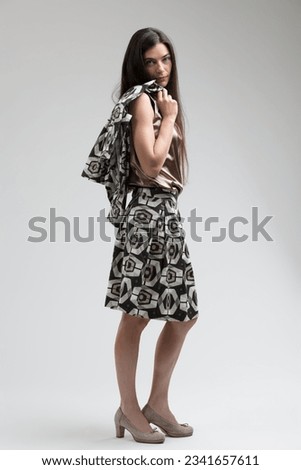 Fashion model poses with blatant haughtiness, seen side-on. Wearing a knee-length dress, a jacket draped over her shoulder, half-heeled shoes, her gaze is vain, scorning those less stunning than her Stock photo © 