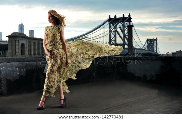 セクシーなポーズを取るファッションモデル 屋上のロケ地に長いイブニングドレスを着て 背景に金属製の橋構造を持つ の写真素材 今すぐ編集