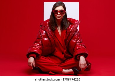 Fashion Model In Red Suit, Down Jacket And Sunglasses. Studio Shot.