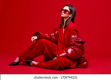 Fashion Model In Red Suit, Down Jacket And Sunglasses. Studio Shot.