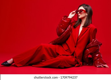 Fashion Model In Red Suit, Down Jacket And Sunglasses. Studio Shot.