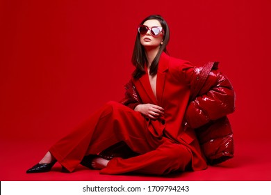 Fashion Model In Red Suit, Down Jacket And Sunglasses. Studio Shot.