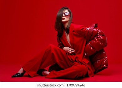 Fashion Model In Red Suit, Down Jacket And Sunglasses. Studio Shot.