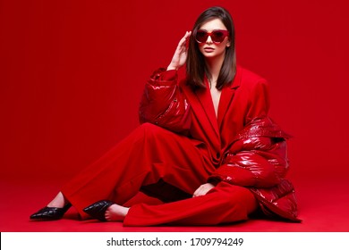 Fashion Model In Red Suit, Down Jacket And Sunglasses. Studio Shot.