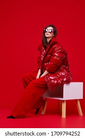 Fashion Model In Red Suit, Down Jacket And Sunglasses. Studio Shot.