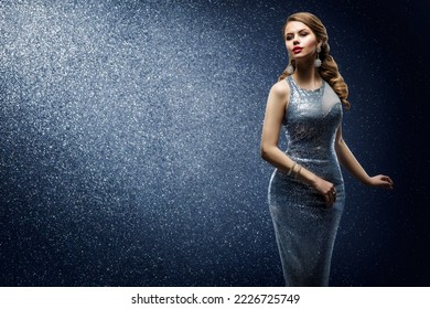 Fashion Model in Silver Sequin Dress. Sexy Girl in Evening Glitter Gown dancing in Spotlight. Beautiful Woman with Glamour Hairstyle and Makeup over Dark Blue shining Background
