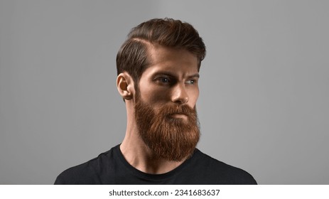 Modelo de moda con pelo y barba elegantes. Hombre con barba larga y bigote en cara seria aislado de fondo gris. Moda y belleza de barbero.