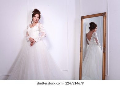 Fashion Model in traditional long lace White Dress gown posing in studio with minimalist background next to big mirror.
 Boudoir dress in the interior Studio. White minimalism for the bride. - Powered by Shutterstock