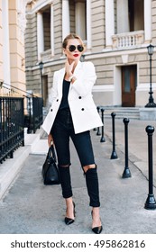 Fashion Model Is Walking On Street On Heels. She Wears Sunglasses, Ripped Black Jeans