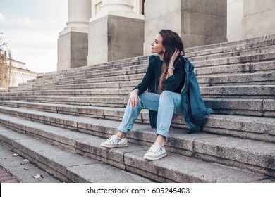 Fashion model wearing ripped boyfriend jeans, jacket and sneakers posing in the city street. Fashion urban outfit. Casual everyday clothing style.