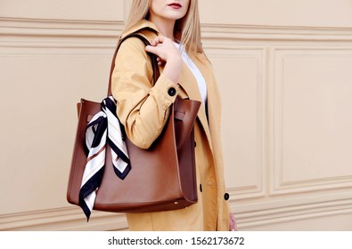 Fashion model woman in autumn outfit with big brown bag scarf. Trendy beige coat