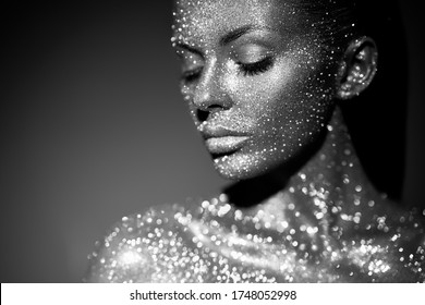 Fashion model woman in bright sparkles and lights posing in studio. Portrait of beautiful sexy woman. Art design glitter glowing make up. Black and white photography