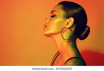 Fashion model woman in colorful bright lights with trendy makeup . Beautiful girl with earrings  jewelry  Beauty and accessories. Neon  and orange with green color