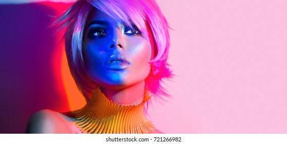 Fashion model woman in colorful bright lights, portrait of beautiful party girl with trendy make-up, haircut. Art design of disco dancer, colorful make up. Over colourful vivid pink background,