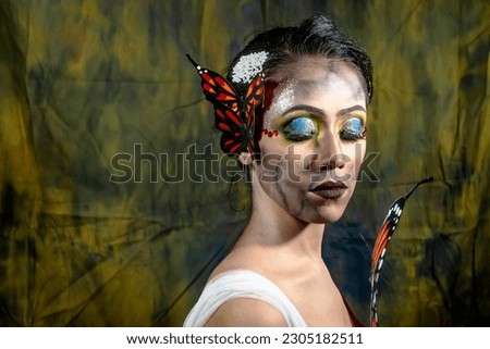 Fashion model woman in lights posing in studio. Portrait of beautiful woman with butterfly. Art designs glitter glowing make up.