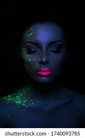 Fashion model woman in neon light bright fluorescent makeup, drop on face. Beautiful model brunette girl colorful make-up, painted skin, body art design ultraviolet