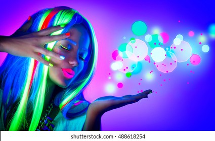 Fashion model woman in neon light, beautiful model girl, painted fluorescent make-up, Body Art design of female disco dancer blowing neon sparks in UV, colorful make up. Gestures for advertisement
