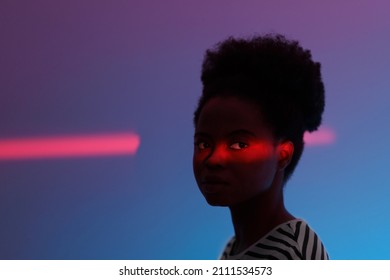 Fashion Neon Light Portrait Of Young African American Woman With High Puff Hairstyle. Silhouette Of Black Millennial Female With Ethnic Hairdo Over Dark Blue Studio Wall With Colorful Light On Face