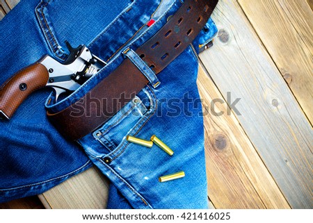 fashion old blue jeans with a leather belt and vintage revolver with cartridges. on a wooden textured background