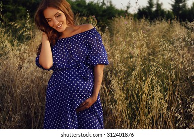 fashion outdoor photo of beautiful pregnant woman with dark hair posing at summer field