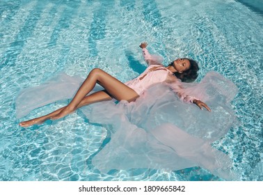 fashion outdoor photo of beautiful sexy woman with dark hair in luxurious dress with accessories posing in swimming pool