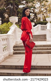fashion outdoor photo of beautiful woman with dark hair in elegant red suit posing in summer park