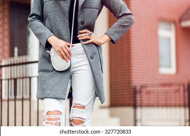 Fashion Outdoor Portrait Of Pretty Young Blonde Woman In Fall Casual Outfit Grey Coat , White Trendy Torn Jeans. Attractive Lady Walking On The Street .Warm Colors. Handbag.