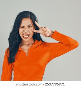 Fashion, peace sign and portrait with woman in studio for winking, gen z and casual style. Trendy, college and education with person on gray background for confidence, tongue out and University pride