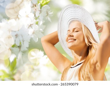 Fashion, People And Summer Holidays Concept - Beautiful Woman In Hat And Dress Sunbathing Over Green Blooming Garden Background