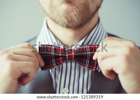 Fashion photo of a bearded man correcting his tie or bowtie. Party, costume wearing, businessman or gentleman concept. Male in vest and shirt correcting his colorful tie. High quality image