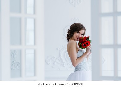 Fashion photo of a beautiful bride with flowers bouquet in her hands at the light room next to the doors