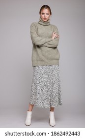 Fashion Photo Of A Beautiful Elegant Young Woman In A Pretty Pale Green Sweater, Gray Long Skirt With Patterns, White Boots Posing Over Light Gray Background. Studio Shot, Portrait. Monochrome Colors